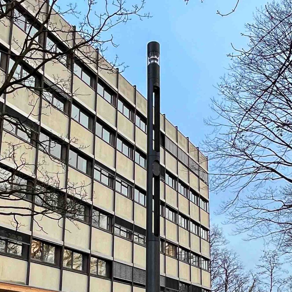 Multifunktionsmast vor einem Bürogebäude bei blauem Himmel.